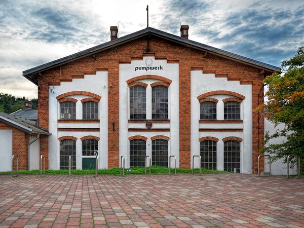 Frontansicht des Kulturzentrums Pumpwerk mit roter Ziegelfassade, weißen Wandflächen und gepflastertem Vorplatz.