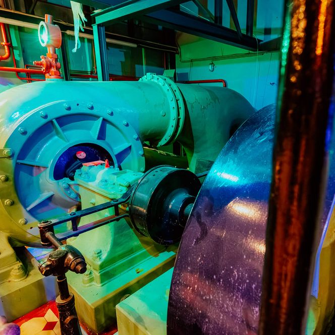 Große historische Wasserpumpe mit Rohrleitungen und Schwungrad im Innenraum eines ehemaligen Pumpwerks.