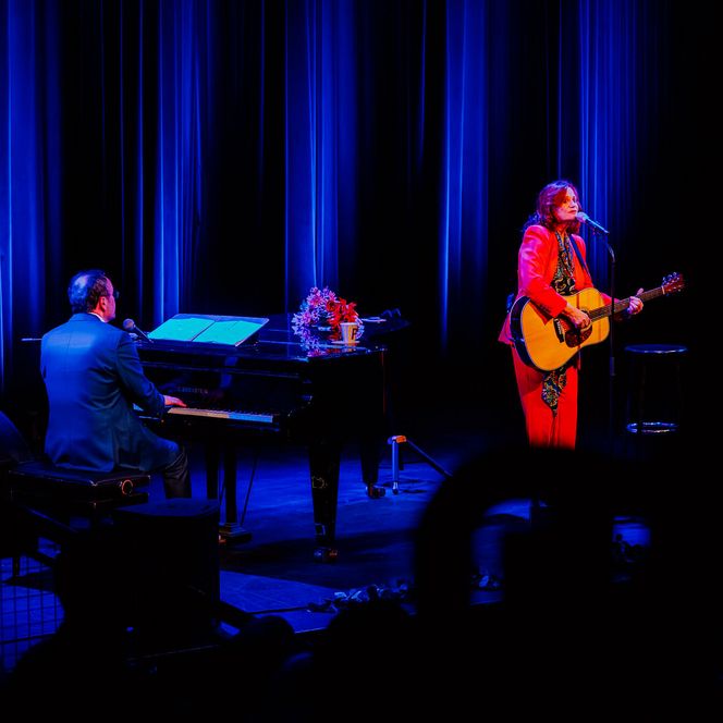 Pe Werner singt mit Gitarre auf einer blau beleuchteten Bühne, begleitet von einem Pianisten am Flügel im Pumpwerk.