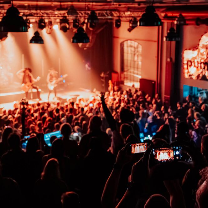 Blick von der Galerie auf ein Konzert im Pumpwerk mit beleuchteter Bühne und Publikum.