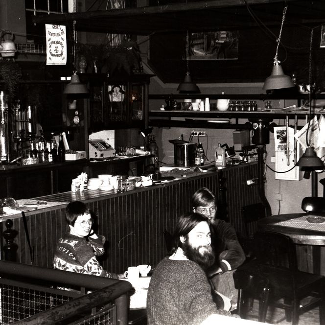 Schwarzweißfoto einer Bar im Kulturzentrum Pumpwerk mit Tresen, Kaffeemaschinen und mehreren sitzenden Gästen.