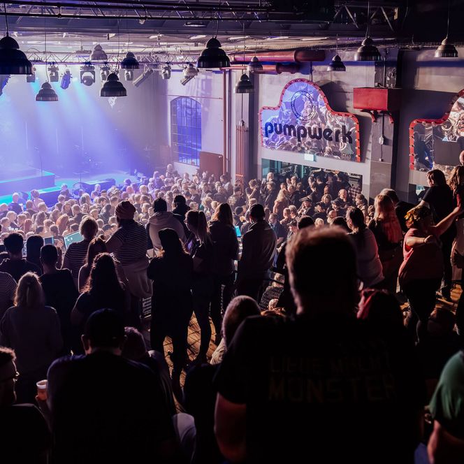 Blick von der Galerie auf ein voll besetztes Konzert im Pumpwerk mit Bühne und Publikum im Saal.