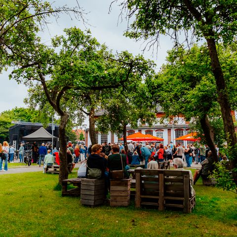 Viele Menschen bei einer Open-Air-Veranstaltung am Pumpwerk mit Bühne, Bäumen und Sitzplätzen auf der Wiese.