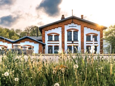 Kulturzentrum Pumpwerk mit weißen Fassaden und großen Fenstern, davor eine Wiese im Abendlicht.