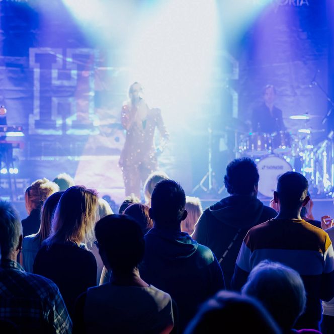 Blick aus dem Publikum auf eine beleuchtete Bühne mit Band und Sängerin bei einem Konzert im Pumpwerk.