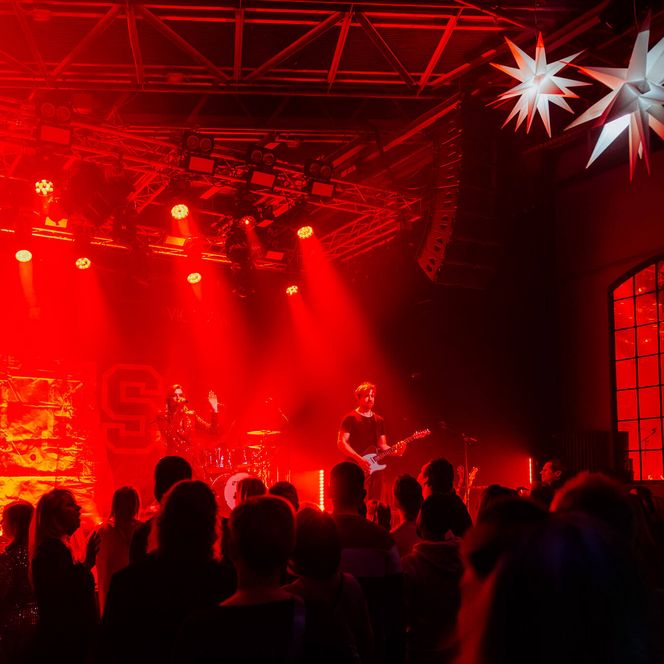 Band auf der Bühne im Pumpwerk, beleuchtet von rotem Licht, Publikum im Vordergrund