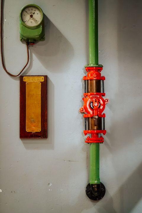 Grüne Rohrleitung mit rotem Ventil sowie Messgerät und Tankanzeige an einer Wand im Pumpwerk Wilhelmshaven.